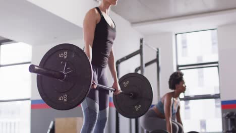 video of two diverse, determined women lifting barbell weights working out at a gym