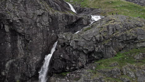 Aerial-shot,-pulling-out-from-a-crashing-waterfall-as-it-rushes-over-a-sheer-rock-face,-near-Trollstigen,-in-Norway