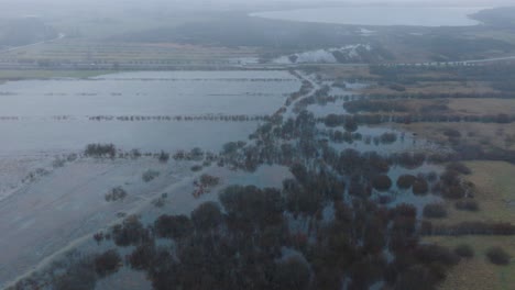 Aerial-establishing-view-of-high-water,-Durbe-river-flood,-brown-and-muddy-water,-agricultural-fields-under-the-water,-overcast-winter-day-with-light-snow,-birdseye-drone-shot-moving-forward