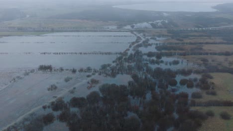 vista aérea de aguas altas, inundación del río durbe, agua marrón y fangosa, campos agrícolas bajo el agua, día de invierno nublado con nieve ligera, disparo de drone de ojo de pájaro avanzando