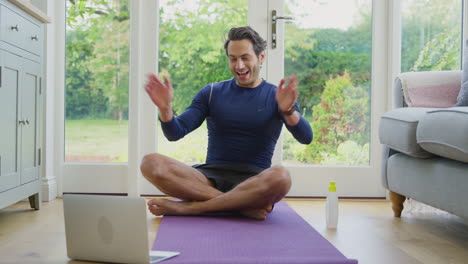mature male teacher sitting on mat at home with laptop giving online yoga class