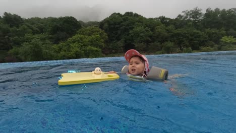 niña de 3 años nadando en piscina al aire libre en un día lluvioso