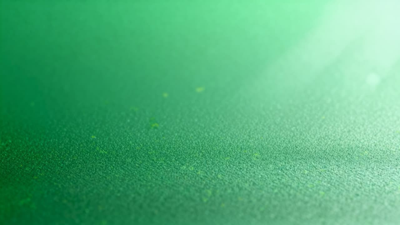 Superfície de feltro verde clareando, reagindo à luz superior direita na mesa, mostrando pontos e reflexo