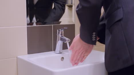 a man in a business suit washes his hands in a public office toilet