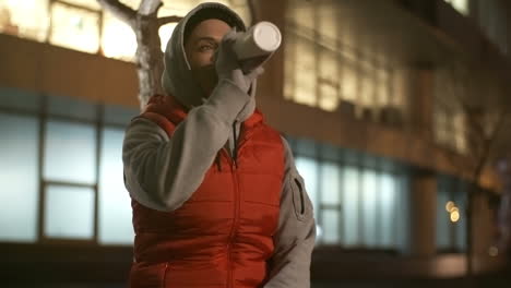 Woman-In-Sportswear-And-Hood-Drinks-Water-Sitting-While-Taking-A-Break