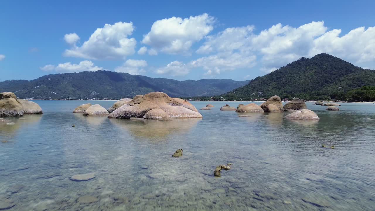 Aerial drone footage of Lamai Beach, Koh Samui, Thailand, showcasing rocky coastline, turquoise ocean water, lush green mountains, and scenic tropical island horizon under a clear sky