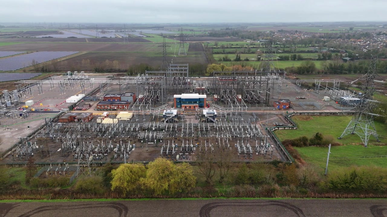 Letecký pohled na masivní elektrickou rozvodnu situovanou vedle velké komerční solární farmy v Burwellu, Cambridgeshire, Spojené království.