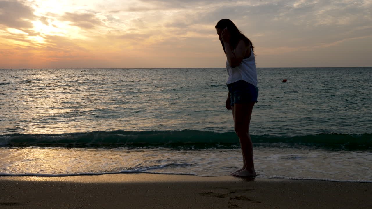 Happy woman on the beach at the sunrise jumping in the water like a child