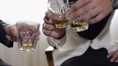 three men in suits toast with glasses of whiskey