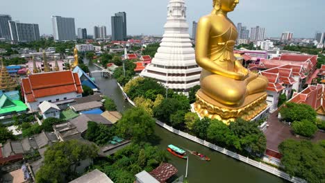 chao phraya river cruise boats passing big golden buddha statue wat paknam bhasicharoen in phasi charoen district in bangkok, thailand - aerial view