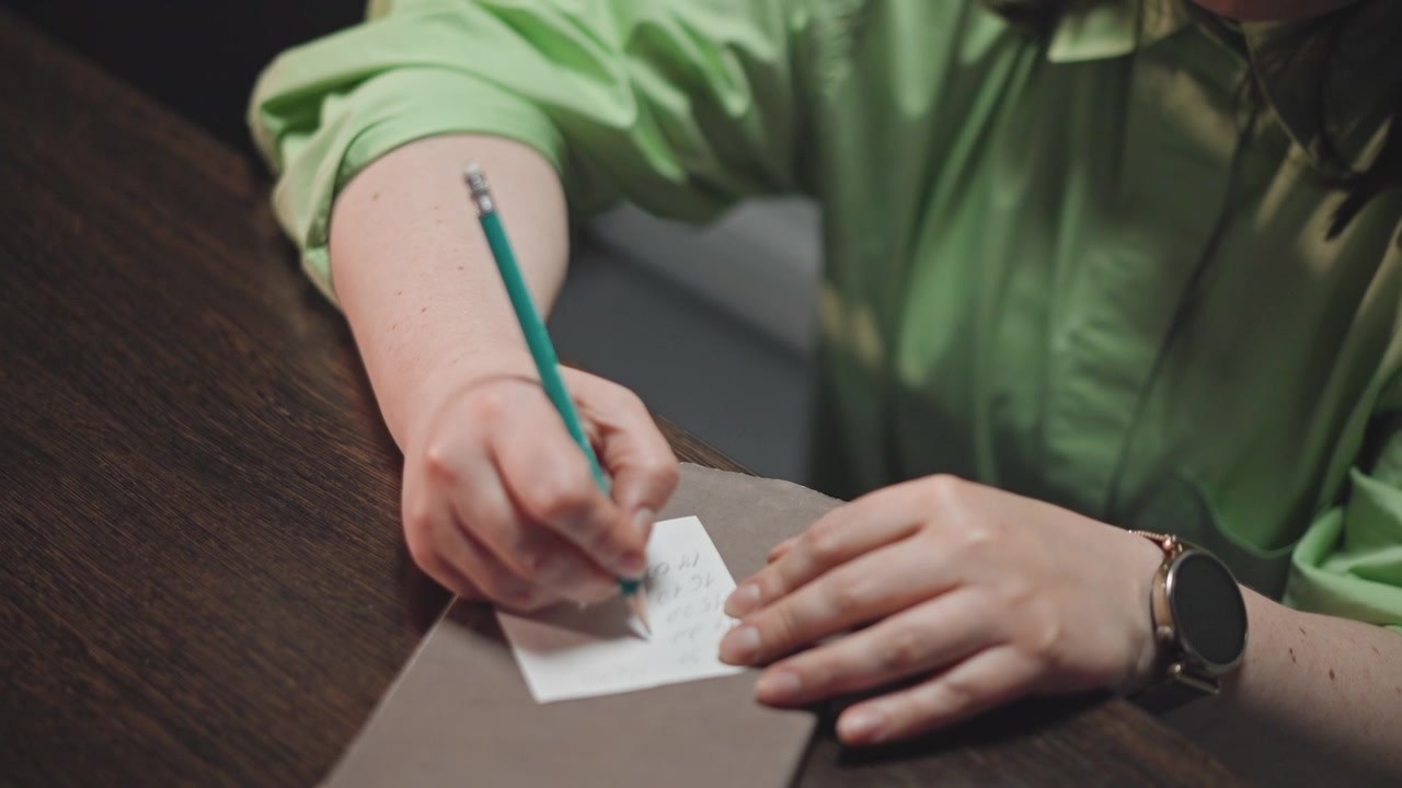 Caucasian educator writing musical notes carefully. Music instructor jotting down notes at wooden desk. Teacher wearing green shirt focusing on composing melody and planning lessons diligently
