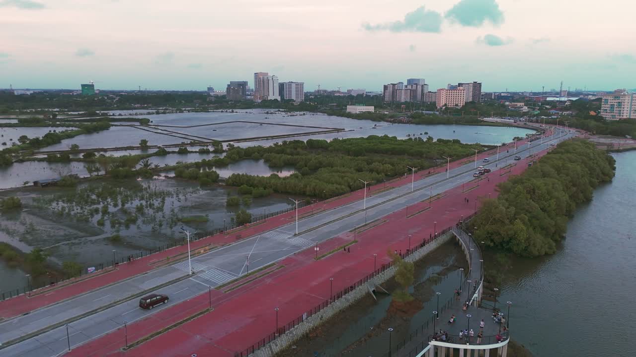 Aerial view of a coastal road alongside wetlands and mangroves with a modern city skyline at sunset. Perfect for travel, urban, and environmental projects