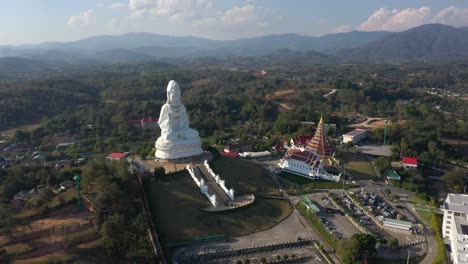 backwards aerial drone of wat huay pla kang giant white big statue and pagoda temple with mountains and landspace in chiang rai, thailand