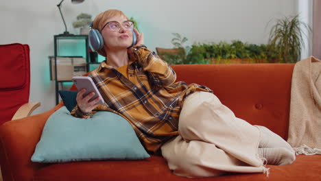 mujer joven feliz con auriculares inalámbricos relajándose acostada en el sofá en casa escuchando su música favorita