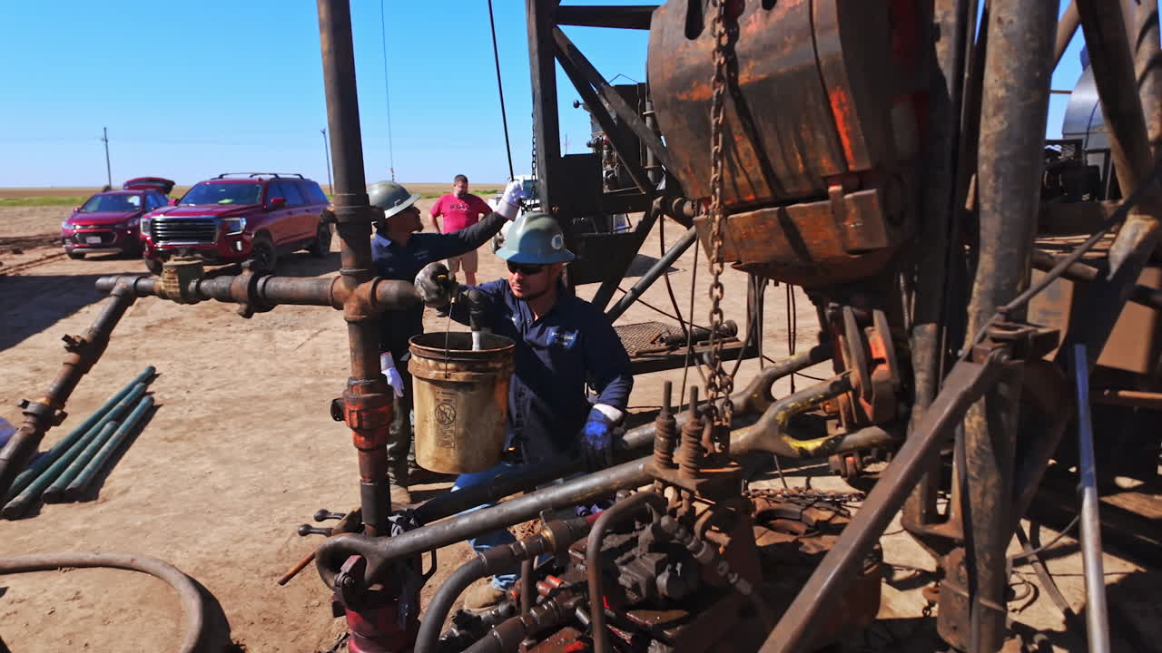 Worker in protective helmet filling the bucket hanging on the pipe with water. Producing oil or gas in the desert.