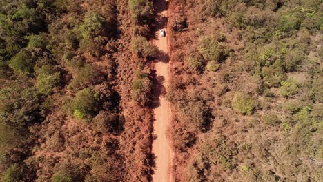 Orbital-view-of-a-moving-car-raising-dust-on-a-dirt-road-in-Chapada-dos-Veadeiros,-Goiás,-Brazil