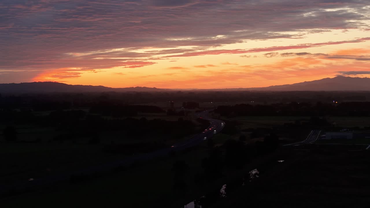 Time-lapse aerial of highway traffic in Hamilton, New Zealand at sunset. Flowing car lights and evening sky create a dynamic urban motion scene