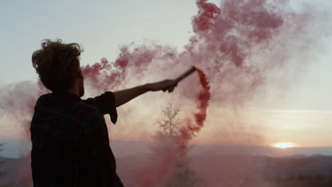 mann tanzt in den bergen bei sonnenuntergang mit rauchflamme