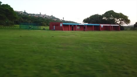 Drone-flying-low-over-cricket-training-nets-and-an-abandoned-old-building-change-rooms-with-a-white-score-board-over-a-rugby-field-Harlequins-on-the-Bluff-in-Durban