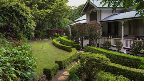 smooth cinematic descending reveal shot,through lush foliage, of a classic traditional country queenslander house, nestling in neatly manicured landscaped garden