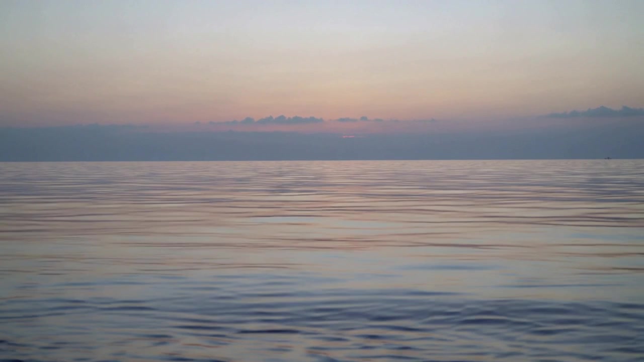 Shifting calm ocean surface moving from swell, showing ripples under pastel sky and low cloud band