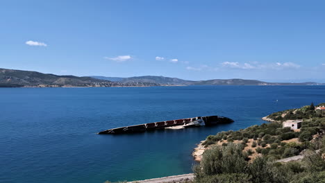 slow motion landscape view of submerged shipwreck ruins wreckage in bay inlet channel sea ocean water with coastline headland mountain region in rural town suburbs travel tourism holidays