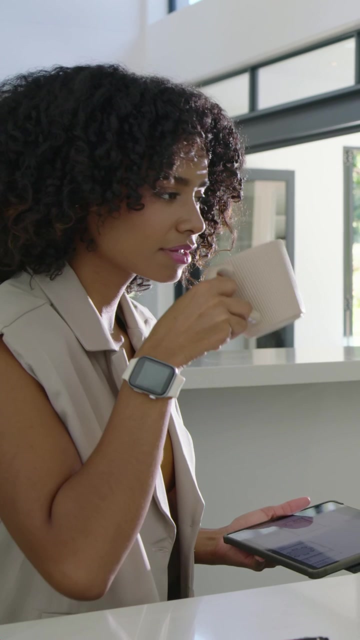 Vertical video: Placing tablet, woman in sleeveless vest leaning at kitchen counter, sipping mug