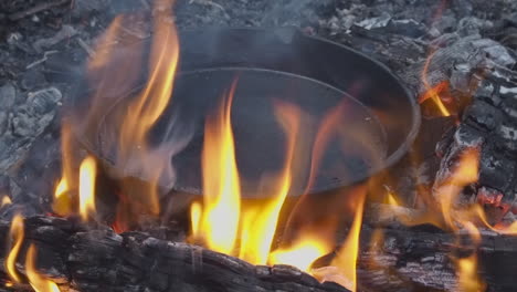 orange flames surround cast iron skillet being seasoned in open fire