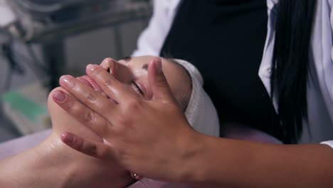 close up view of a woman with her eyes closed lying on the couch during cosmetic face procedure. professional cosmetologist is