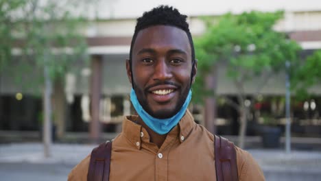 Portrait-of-smiling-african-american-businessman-with-face-mask-in-urban-park