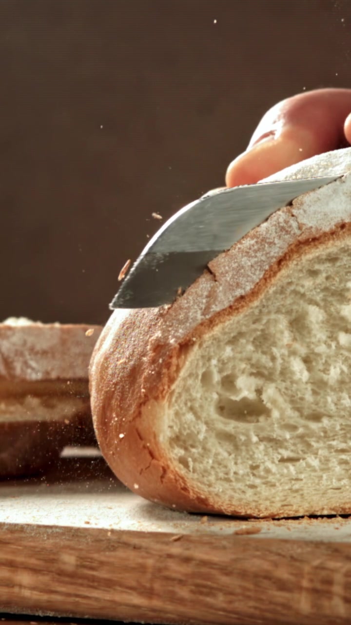 Hand Slicing a Loaf of Fresh Bread on a Wooden Board