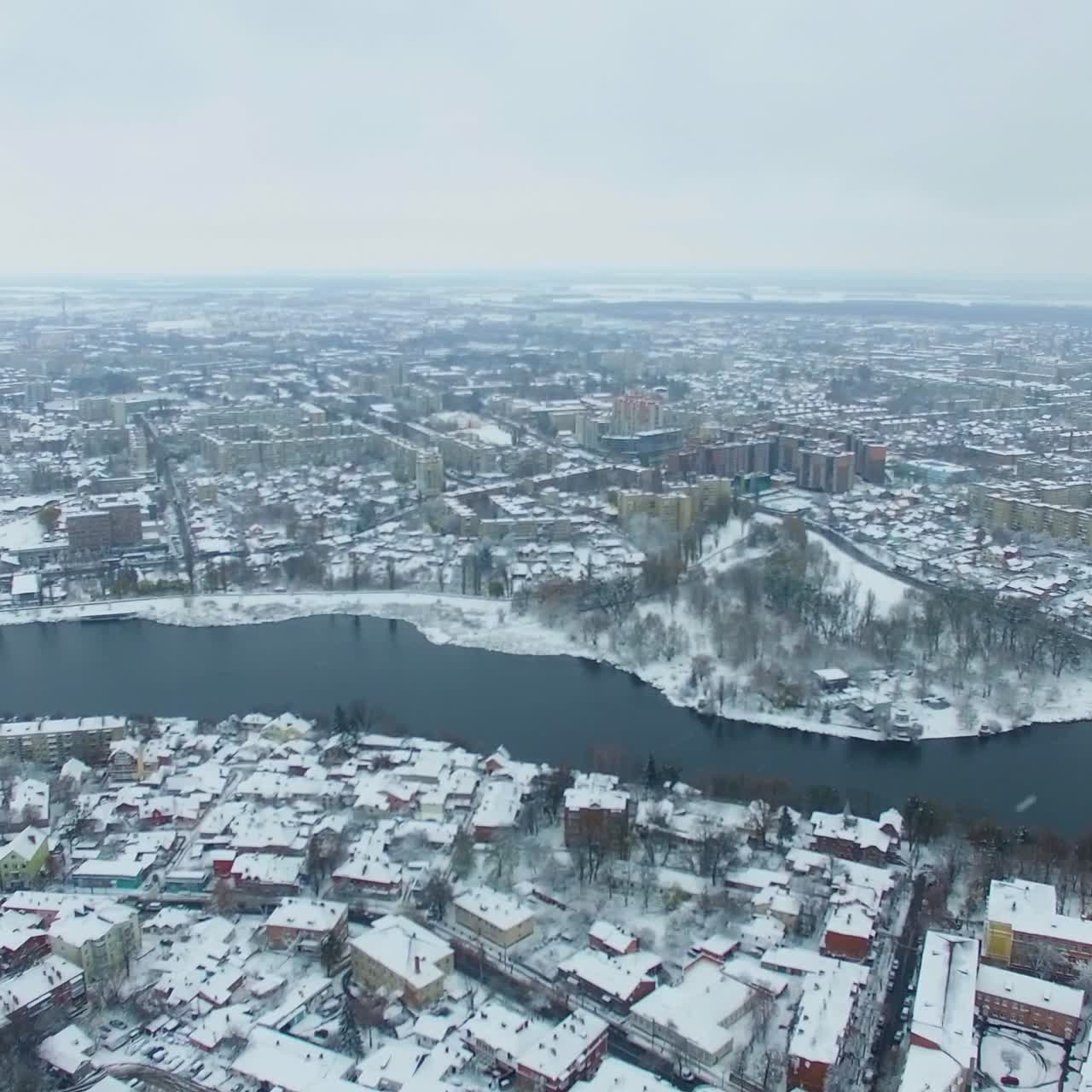View of the big city with river floating through it on snowy winter day. Vast panorama of the city covered with snow. Top view