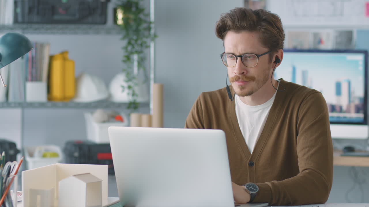 arquitecto masculino en la oficina escuchando música en auriculares inalámbricos mientras usa una computadora portátil