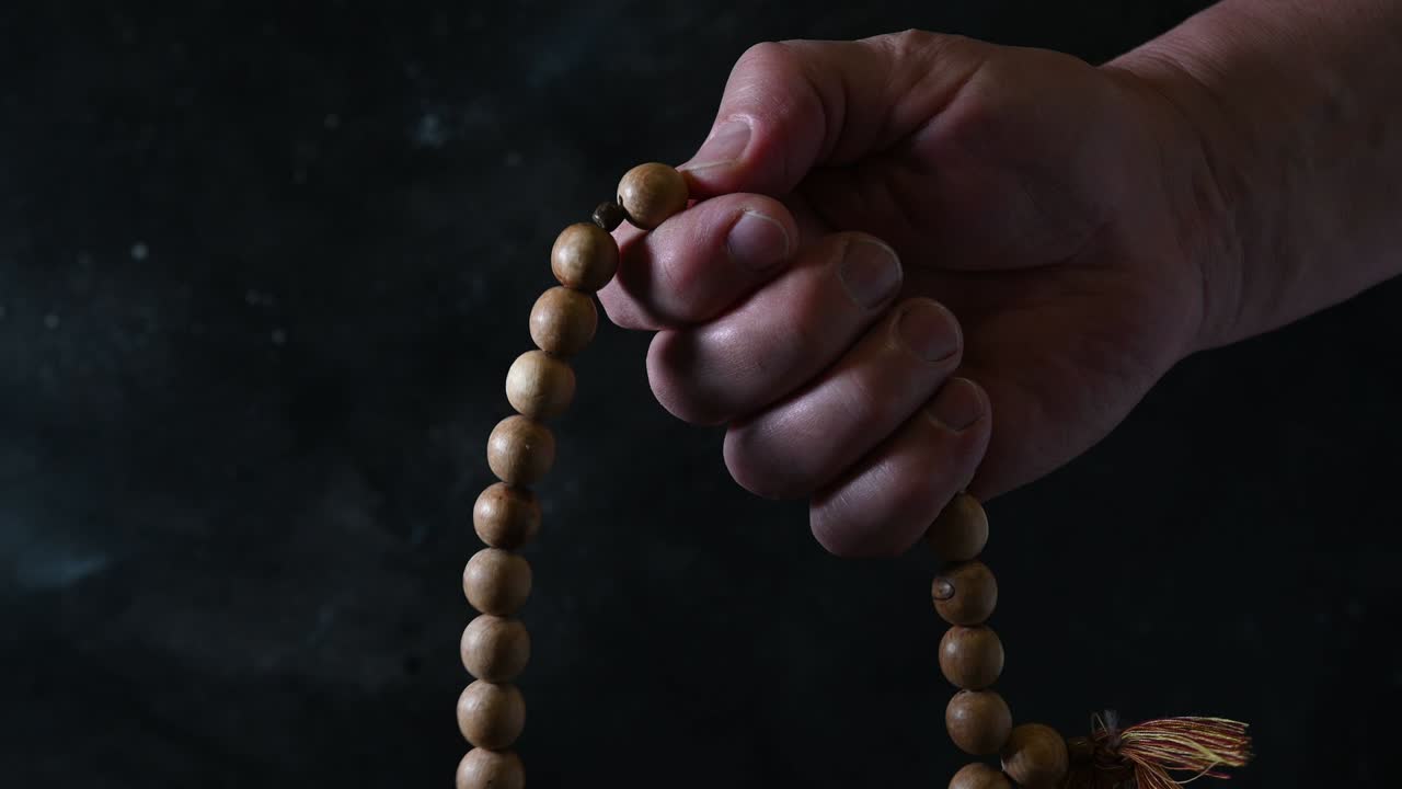 cuentas de oración de madera en la mano del hombre en la oscuridad. tradición religiosa.