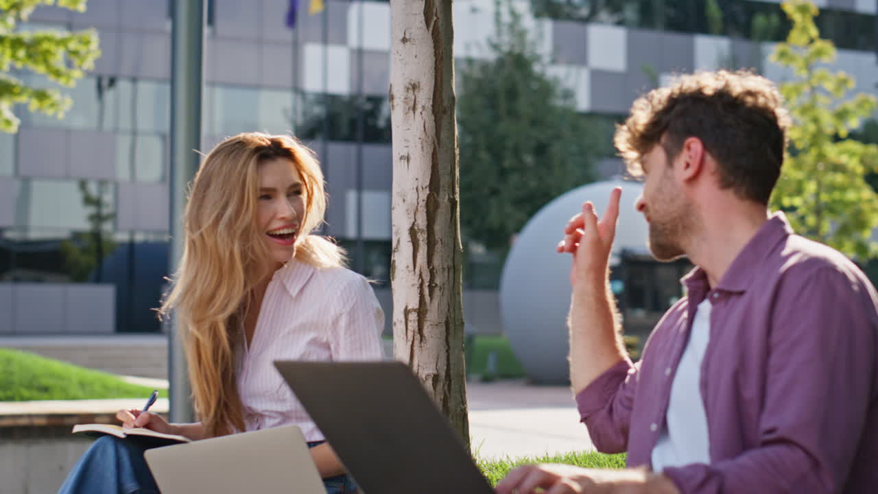 amigos riendo en un parque urbano de primer plano. una pareja sonriente trabajando remotamente charlando