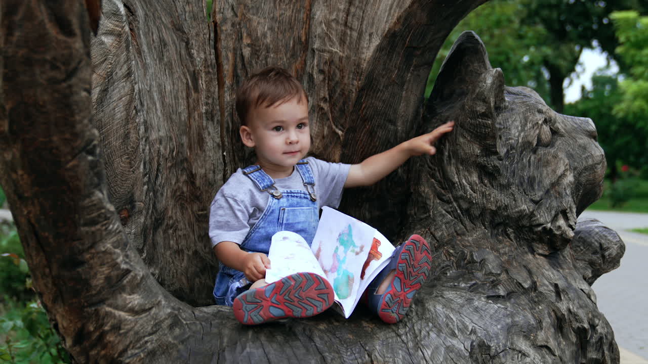 Toddler Reading a Book in a Park by a Wooden Cat Sculpture