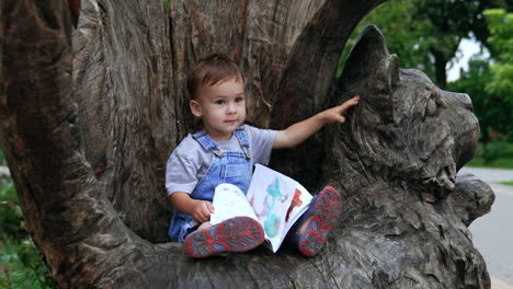 toddler reading a book in a park by a wooden cat sculpture