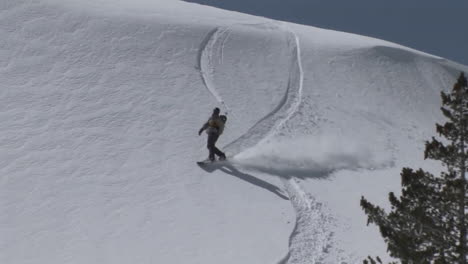 Following-shot-of-a-snowboarder-as-he-boards-slowly-down-a-slope-of-virgin-powder