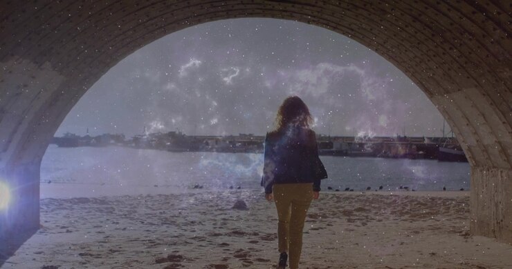 Eine Frau tritt durch einen Ziegelbogen auf einen Strand, wobei ein technologisches, kosmisches Overlay um sie herumwirbelt.