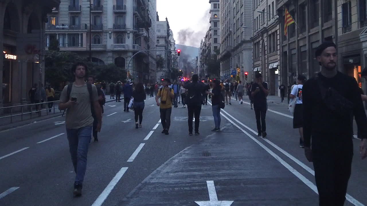 People on Via Laietana in Barcelona during the Catalan protest with a big fire and black smoke in the background. Shot in slow motion.