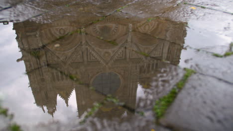 panning view of imposing church reflects in puddle