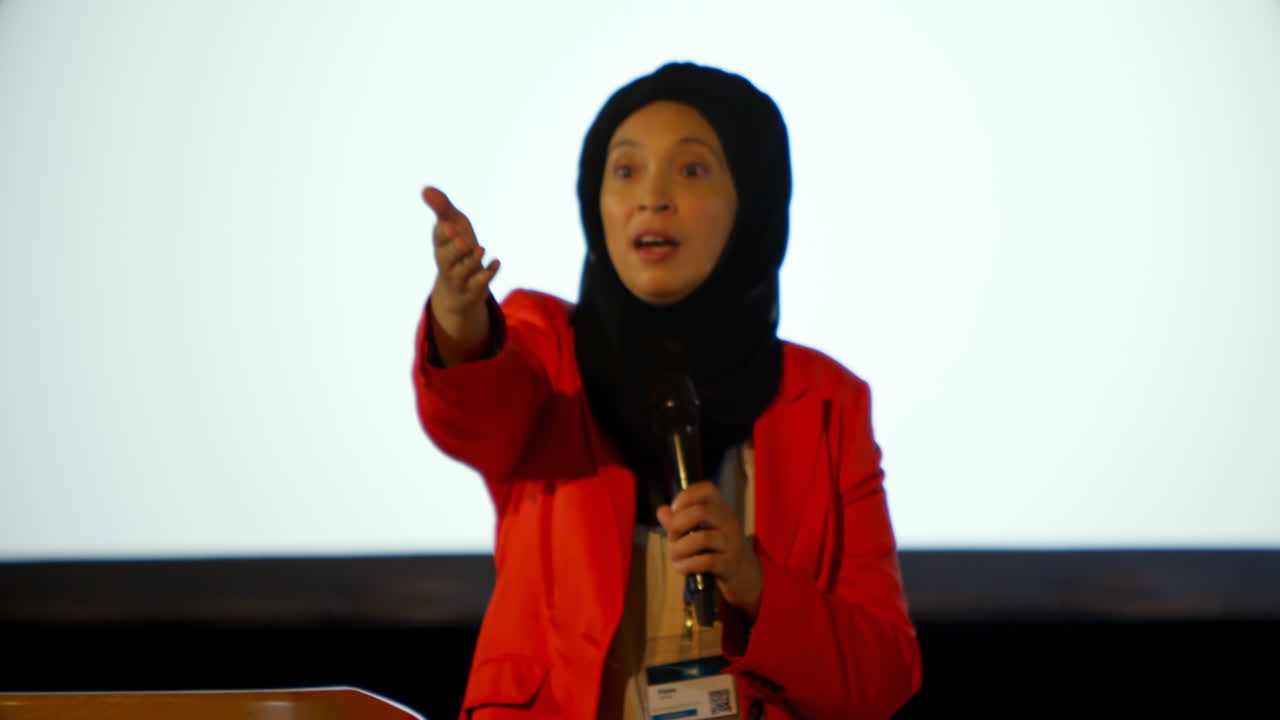 Mature Caucasian hijab businesswoman speaking at podium in auditorium 4k