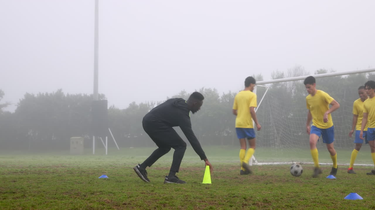 Playing soccer, coach training young players on foggy field with goalposts