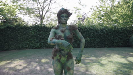 brede opname van een vrouwelijk model met groene bodypaint die langzaam in de natuur loopt en danst, in de stijl van door de natuur geïnspireerde vormen