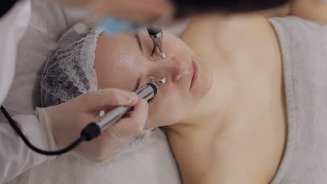 middle-aged woman receiving micro currents facial skin treatment from beautician in spa clinic