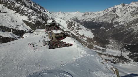 aerial,-rocky-house-in-the-swiss-alps,-snowy-mountain-and-blue-sky