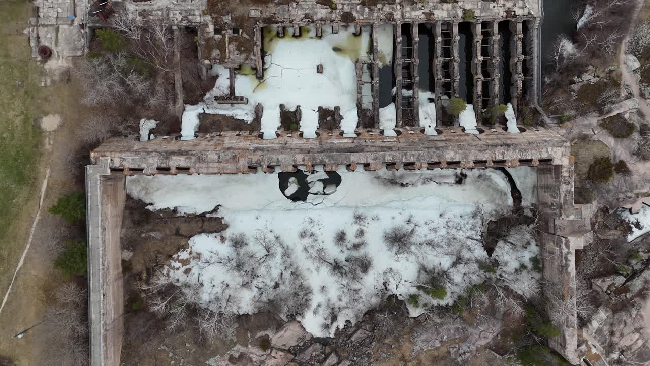 Drone aerial flyover of the historic Pinawa Dam in Manitoba’s Heritage Park during spring. Snow remains on the ground, with surrounding boreal forest, river, and the old hydroelectric ruins in view