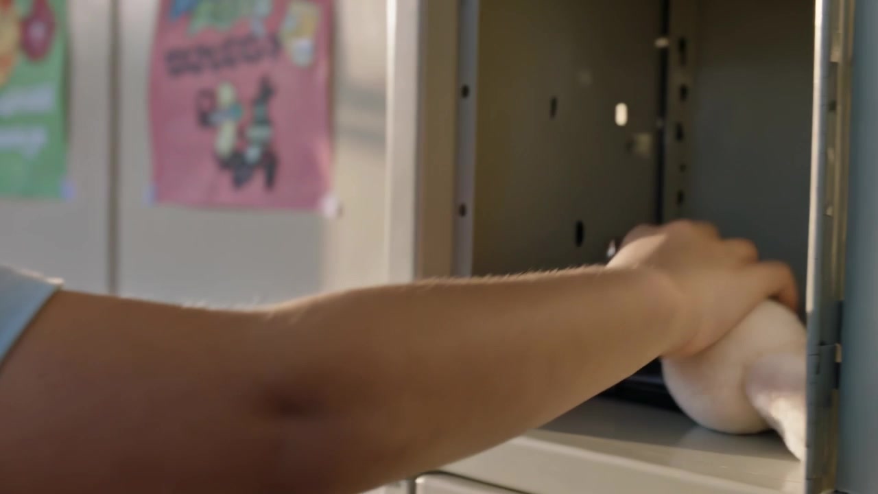 Reaching child unclipping plush from gray backpack in school locker, placing toy inside, copy space