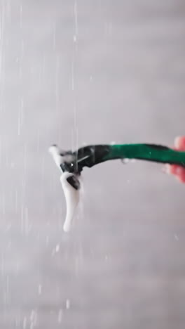 woman washes razor from foam under shower drops in shower closeup. lady cleans shaver with water sprays in bathroom. personal hair removal supplies