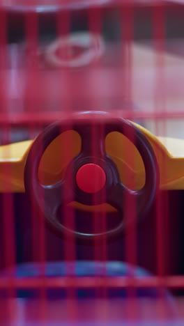 a close-up view of the interior of a children's shopping cart designed like a car, featuring a colorful steering wheel and vibrant yellow and red hues